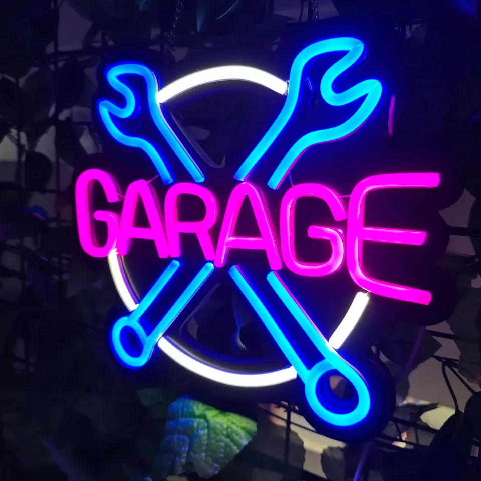 A GARAGE neon sign with crossed spanners, lit against a dark wall